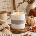A lit jar candle labeled 'FALL SUNDAY' by Salt House Lane, styled on a wooden tray with autumn leaves, pumpkins, a knit blanket, a mug, and a framed quote in a warm home setting.