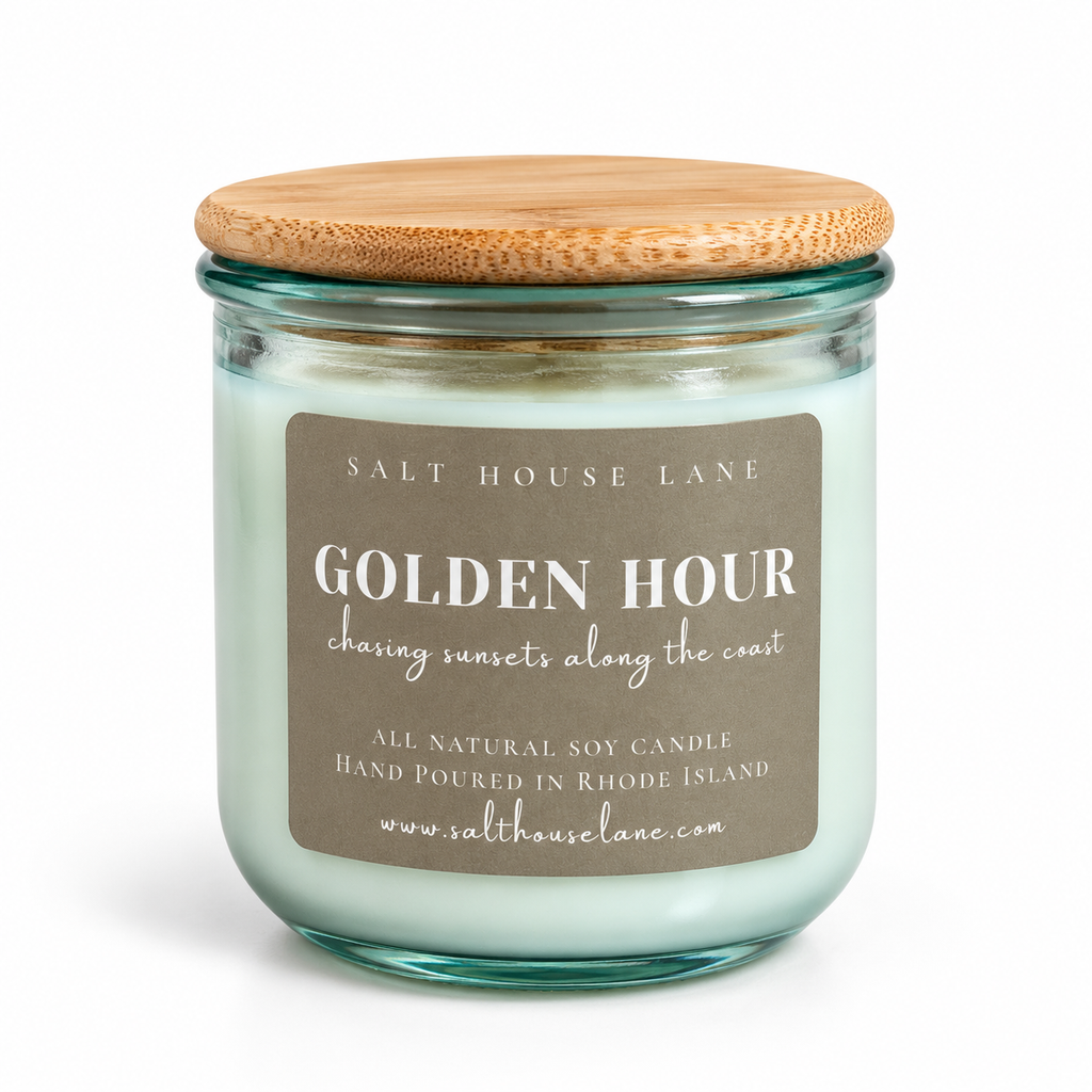 A salt house lane soy candle in a clear glass jar with a light wood lid, featuring a sage green wax and a brown label that reads 'GOLDEN HOUR'.