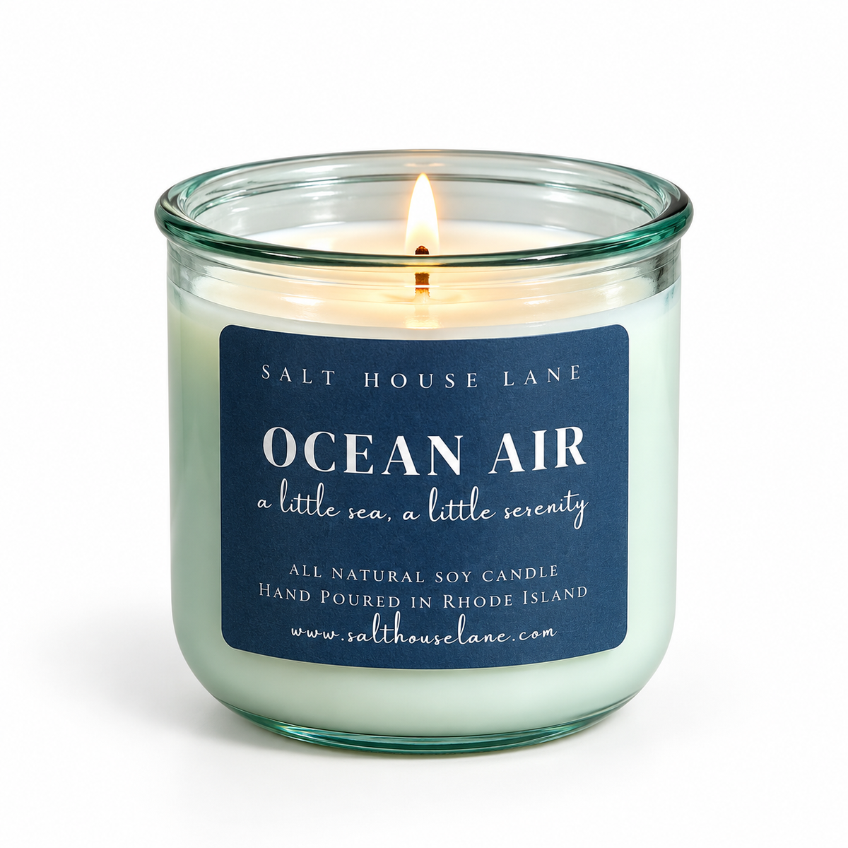 A lit salt house lane 'Ocean Air' soy candle in a clear glass jar with a dark blue label, set against a plain white background.
