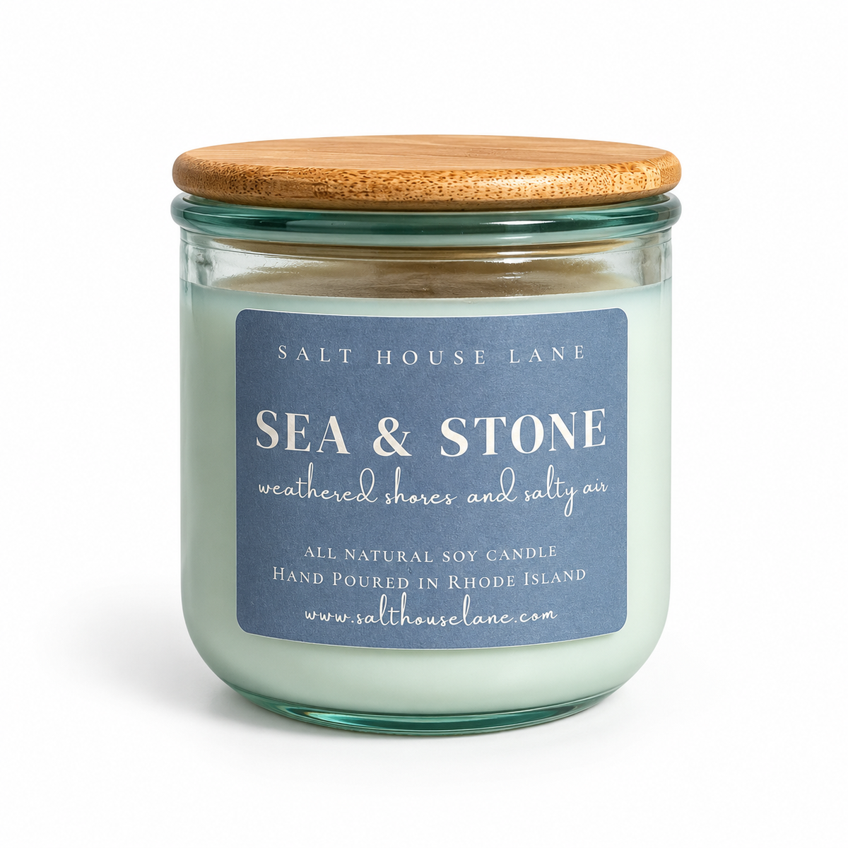 A glass jar candle with a light wood lid and a blue label reading 'SEA & STONE' by Salt House Lane, shown on a white background.